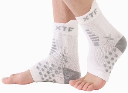Two feet wear Faire.com's Targeted Pain Relief Ankle Sleeves (1-PAIR) in white, featuring gray grip patterns and "XTF" near the top, designed to help reduce ankle swelling and provide moisture-wicking comfort.