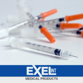 Several Exel U-100 Comfort Point Insulin Syringes 1cc x 28g x 1/2" (Box of 100) by MedPlus, featuring orange caps and smooth plungers, are scattered on a white surface above the Exelint Medical Products logo. Price: $14.38 per box from 6/24/25.