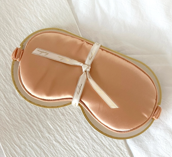 A comfortable Satin Sleep Mask by LoveLina for relaxation on a white bed.