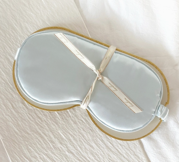 A comfortable blue Satin Sleep Mask by LoveLina on a peaceful white bed.