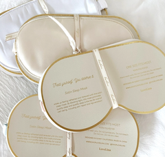 A set of Satin Sleep Masks by LoveLina in white and gold, providing comfort for a peaceful night's sleep on a white bed. (Sold by Faire.com)